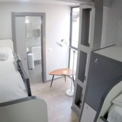 Interior de dormitorio con camas individuales y literas en tonos gris y blanco en el Hostel Quarter de Bilbao
