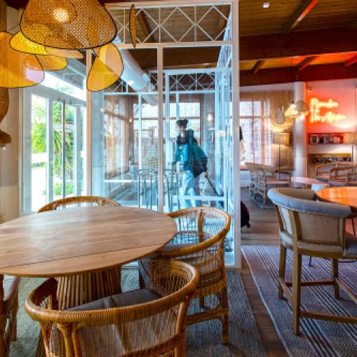 Interior del bar cafetería con mesas de madera  y mimbre del hotel Ibis de Valencia