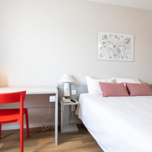 Dormitorio doble con cama y mesa blanca y silla roja en el Hotel Ibis de Valencia